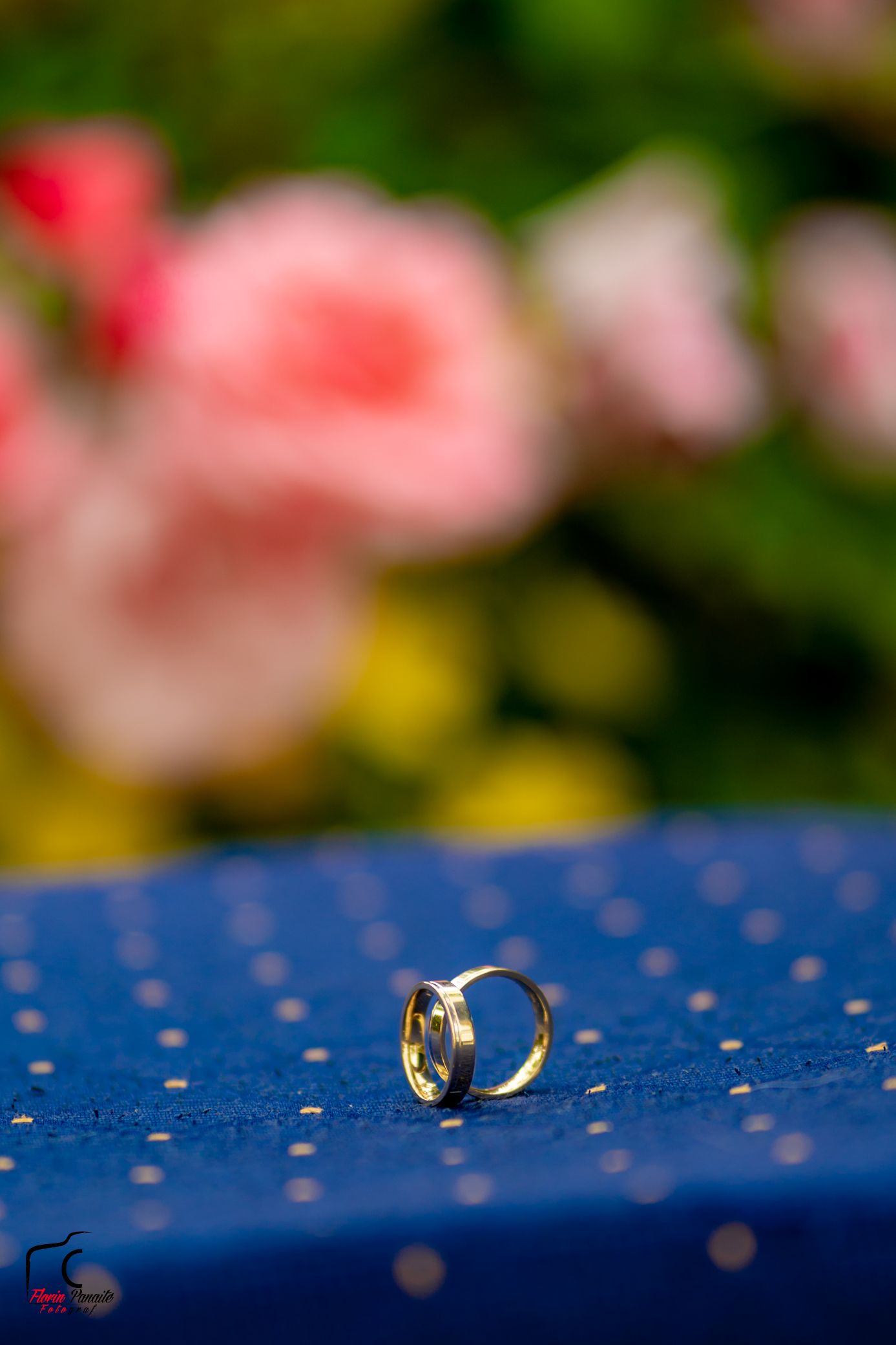 Wedding rings photographed on blue surface with water droplets and soft floral background.