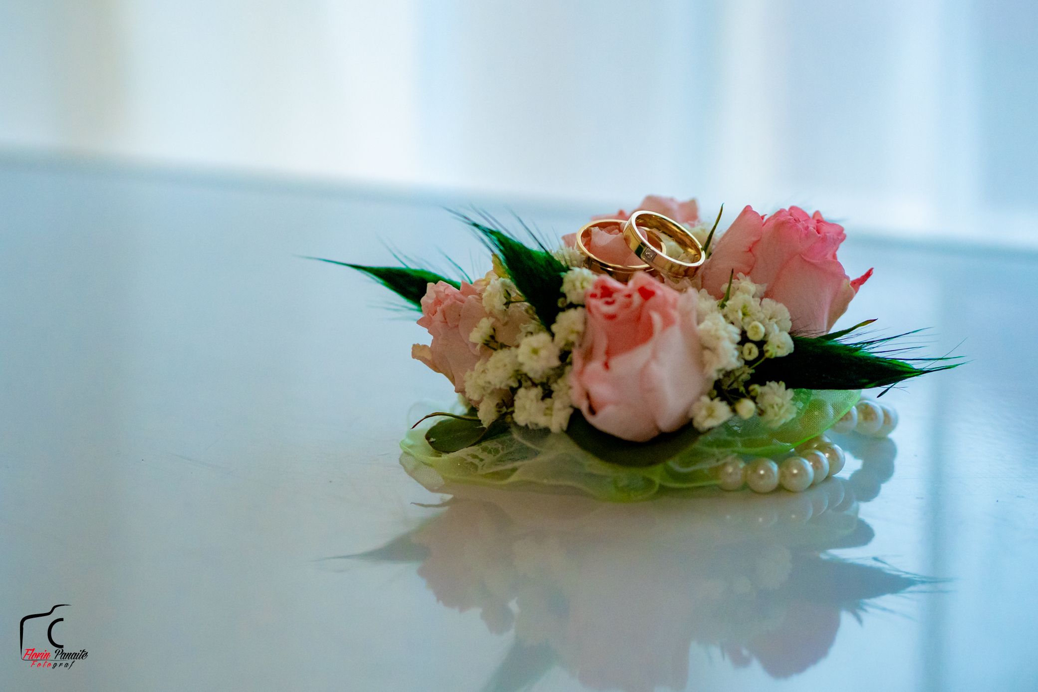 Wedding corsage with pink roses and baby's breath lying on a white reflective surface.