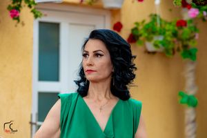Woman in emerald green dress poses elegantly against yellow wall with red roses and greenery.