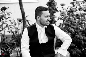 Black and white portrait of man in formal attire smiling outdoors.