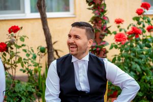 Man in vest and white shirt laughs joyfully near rose garden.