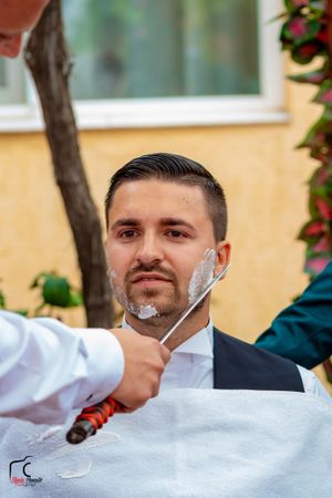 Close-up of groomsmen helping adjust formal attire during outdoor wedding preparations.