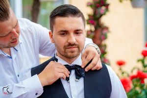 Wedding party helps with formal attire adjustments during outdoor photo session.
