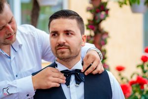 Wedding party members help adjust formal attire during outdoor preparations.