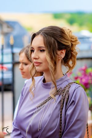 Person in purple dress with styled hair at outdoor event.