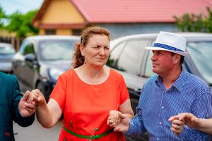 Wedding guests in colorful outfits dance and celebrate outdoors near parked cars.