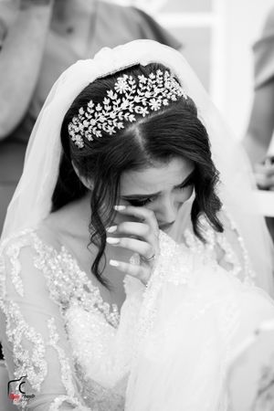 Black and white photo of a bride in a crystal tiara and veil wiping tears from her eyes.