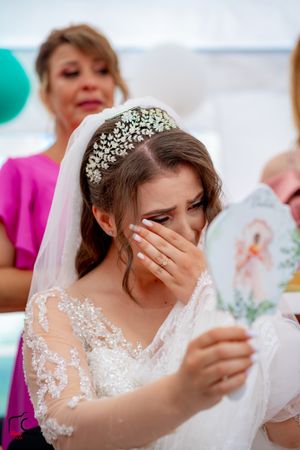 Bride in crystal tiara covers face while reading card at wedding celebration.