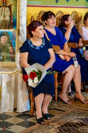 Wedding guests in navy blue dresses seated on ornate chairs during an indoor ceremony.