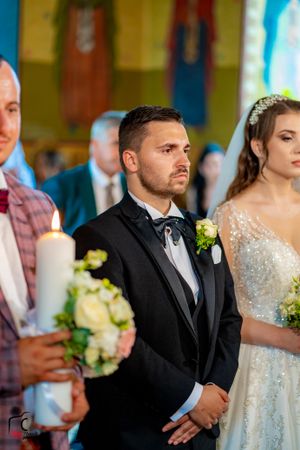 Wedding party members stand formally during traditional church ceremony holding candles and flowers.