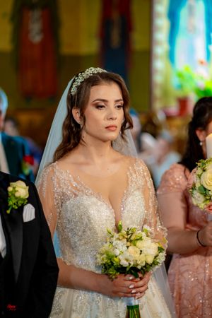 Bride in sparkling white gown and veil holds elegant white bouquet during ceremony.