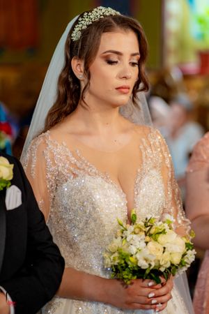 Close-up of bride in embellished white gown and crystal headpiece holding floral bouquet.