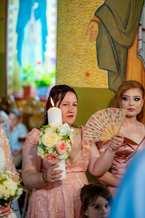 Bridesmaids in peach dresses hold decorative fans during an elegant wedding ceremony.