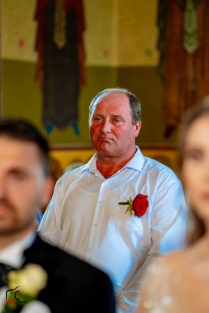 Wedding guest in white shirt with red boutonniere watches the ceremony.