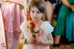 Young attendant in pink dress holds a small red flower during the wedding.