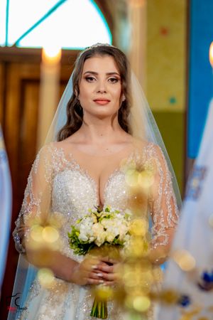 A close-up shot of a bride holding a white bouquet with golden bokeh lights in the foreground.
