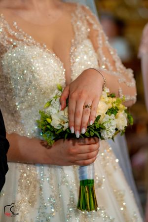 Close-up of a bride's hands holding a white and green bouquet, showing her wedding ring and manicure.