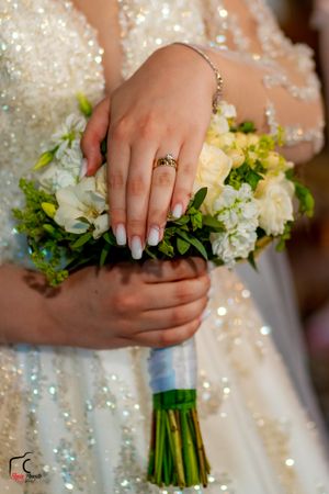 Detailed shot of manicured hands holding a white and green wedding bouquet with sparkly dress detail.