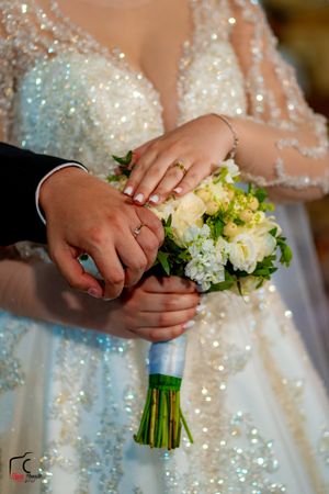 Close-up of hands exchanging rings during wedding ceremony with floral bouquet.