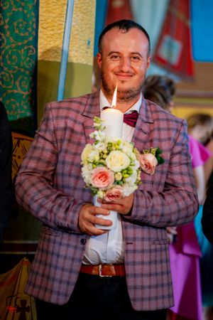 Wedding guest in plaid blazer holding decorative candle and floral arrangement.
