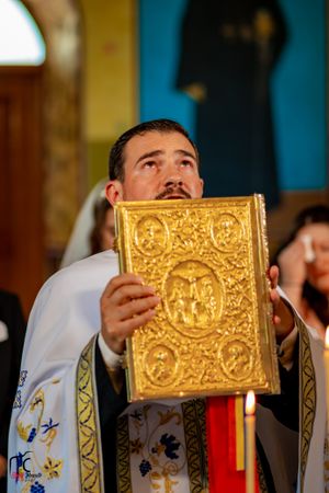 A priest holds up an ornate golden religious book with decorative embossing during a church service.