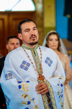 A priest wearing an embroidered white vestment with blue and gold details performs a religious ceremony.