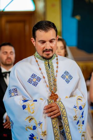 A priest in ceremonial white robes with intricate blue and gold embroidery performs religious rites.
