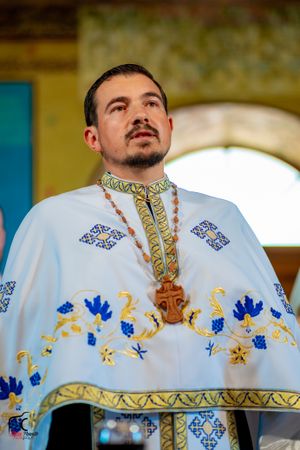 An Orthodox priest in traditional white vestments adorned with blue and gold embroidery conducts a service.