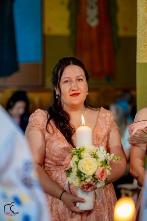 A person in a peach-colored dress holds a white candle during a church ceremony.