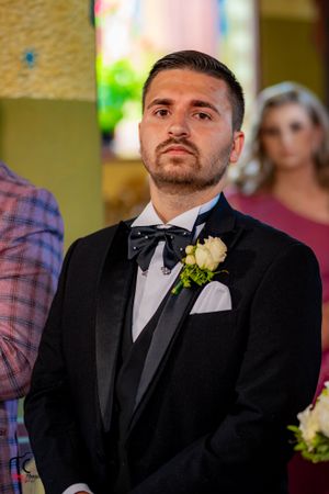 Groom in classic black tuxedo with white boutonniere at wedding ceremony.