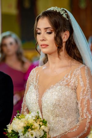 Bride wearing sparkly long sleeve wedding gown with veil holding white and green bouquet.
