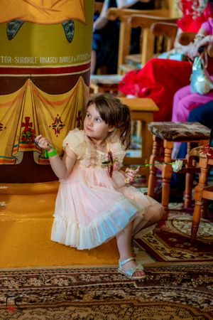 Young child in pink dress sitting on ornate carpet during wedding reception.