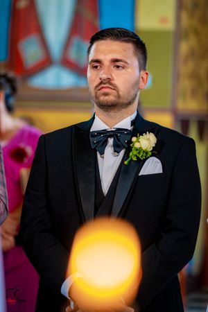 A wedding ceremony in a church with a groom in a black tuxedo standing at the altar.