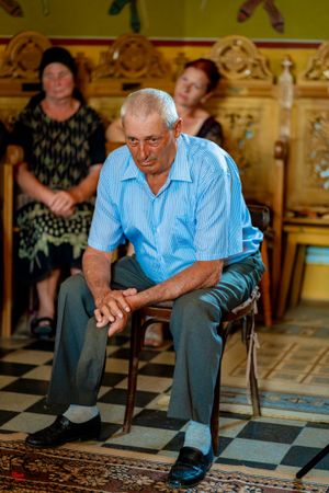 An elderly guest in a blue striped shirt sitting on a wooden chair during a wedding ceremony.