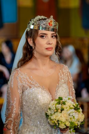 Bride wearing a sparkly wedding gown and crown holding a white and green bouquet.