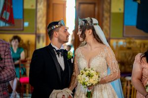 Close-up of wedding couple during Orthodox ceremony with golden crowns and yellow bouquet.