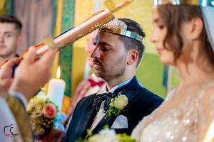 Wedding couple during Orthodox crown ceremony in colorfully decorated church interior.