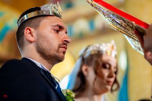 Close-up detail of ceremonial crowns during Orthodox wedding ritual with yellow background.