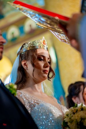 A bride wearing a sparkling dress and crown poses during an Orthodox Christian wedding ceremony.