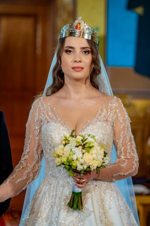A bride in an empire waist beaded gown holds a yellow and white bouquet during her wedding ceremony.