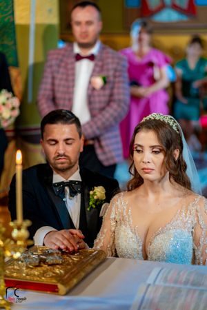 Couple participating in traditional Orthodox wedding ceremony with candles and ornate decorations.
