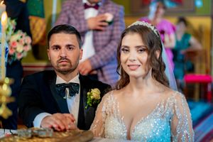 Couple smiling during Orthodox wedding ceremony wearing formal attire and traditional ceremonial crowns.