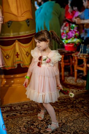 Little girl in pink tulle dress dancing on decorative carpet at wedding celebration.