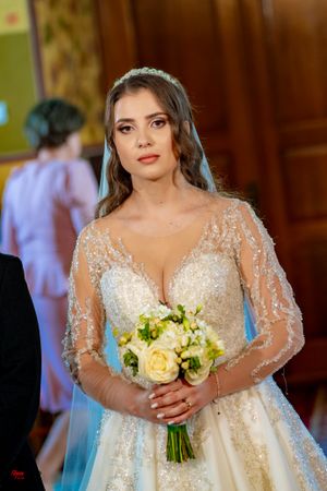 A bride in a sparkling lace wedding gown holds a yellow and white bouquet during her wedding ceremony.