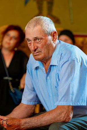 An elderly attendee in a blue striped shirt rests at a celebration venue.