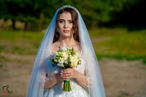 A bride poses with her yellow and white floral bouquet against a natural outdoor backdrop.