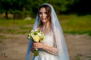 A bride in an elegant white dress holds her bouquet in an outdoor garden setting.