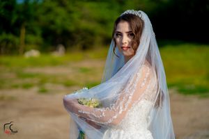 A bride in a white lace wedding dress with veil poses outdoors against a natural green background.