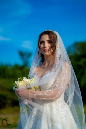 Bride in white dress poses with yellow bouquet against vibrant blue sky background.