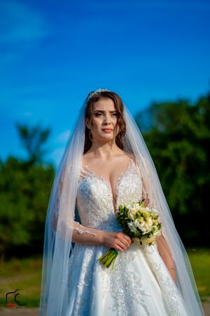 Bride holds yellow and white bouquet while wearing sparkly lace wedding dress outdoors.
